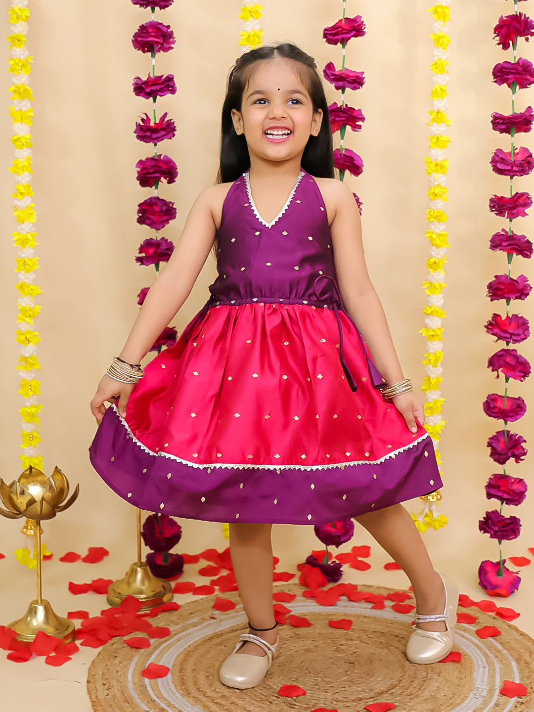 Young girl in a pink and purple dress standing in front of floral decorations.