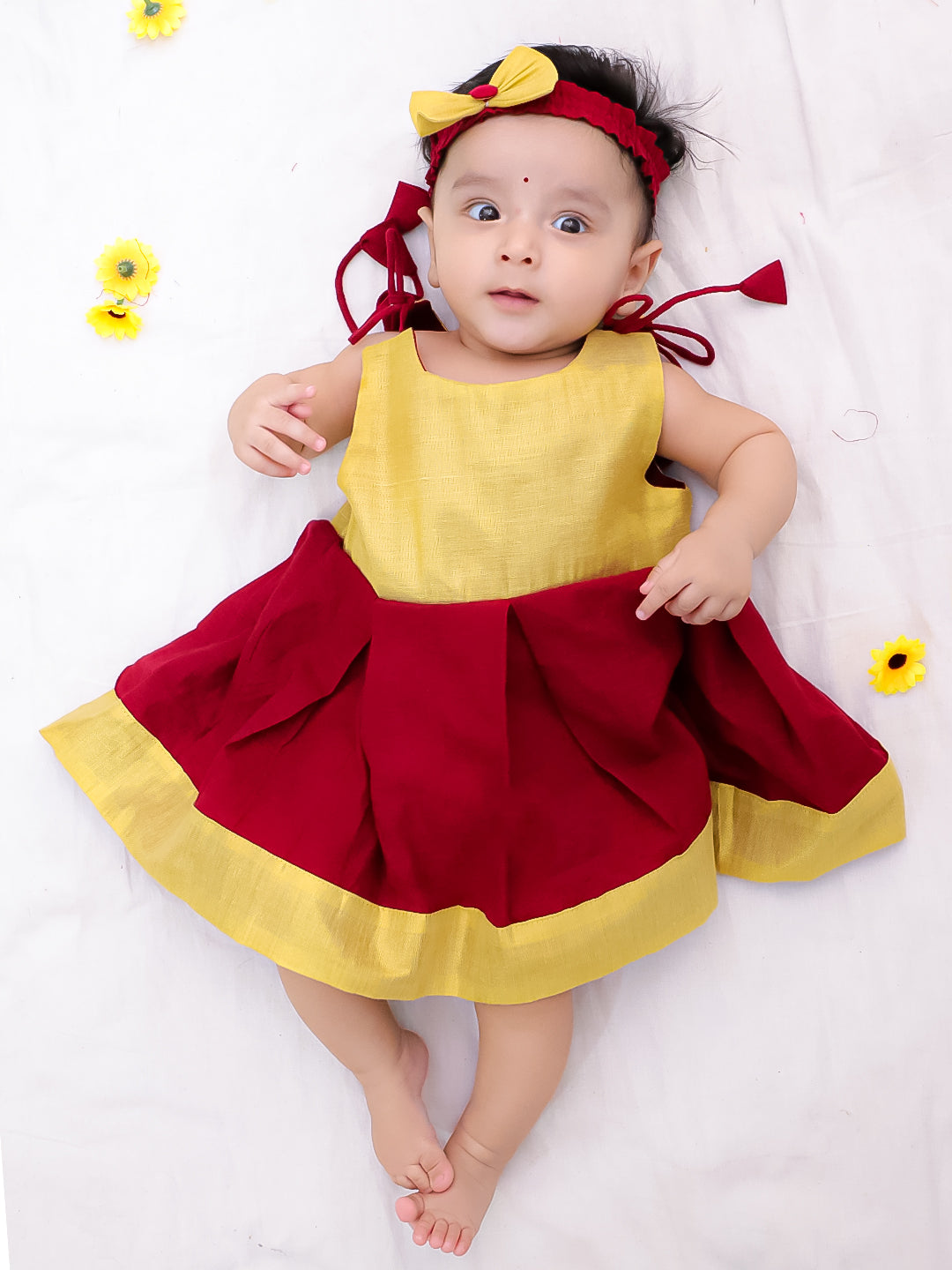 Baby wearing a red and yellow dress with a bow on a white background